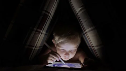 A little boy draws with a stylus on an electronic tablet in a pillow hut Stock Footage 221582895