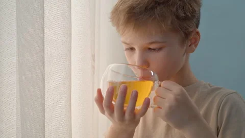 Little boy drinking herbal tea from transparent glass cup at home Stock Footage 329923529