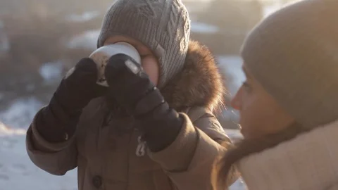 Little boy drinking hot tea during winter walk with his mom in the forest Stock Footage 85633946