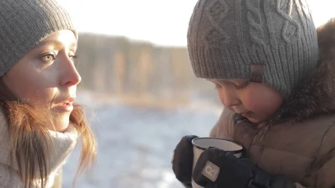 Little boy drinking hot tea during winter walk with his mom in the forest Stock Footage 85633966