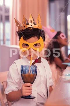 Little boy drinking juice with sipping straw while being at masquerade Stock Photos