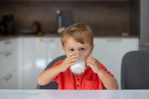 Little boy drinking milk in the morning sitting at the table in the kitchen. Stock Photos