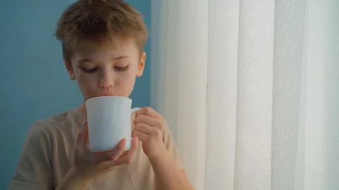 Little boy drinking tea or hot chocolate by the window Video stock 326168126