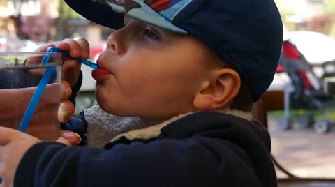 Little boy drinks juice through a straw while sitting at table Video stock 59946101