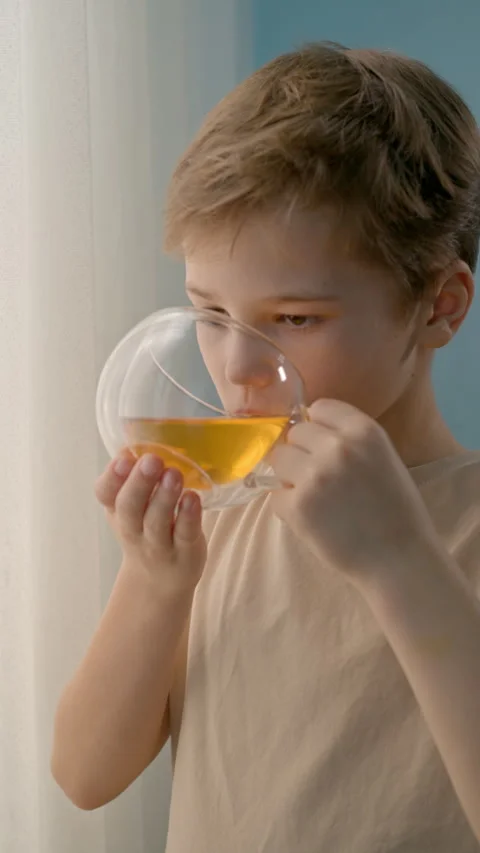 A little boy drinks tea from a clear glass cup at home. vertical video. Stock Footage 330521752