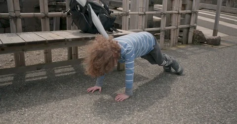 A little boy drops and does push-ups in front of a bamboo fence, the camera pans 库存影片 111688789