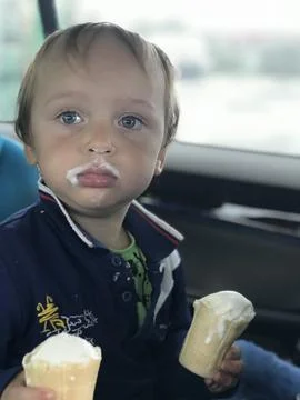Little boy eats 2 ice cream while seats in a car seat. Children sefety in a car Stock Photos