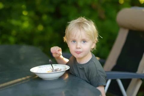 Little boy eats breakfast cereal in the yard of his house. Stock Photos