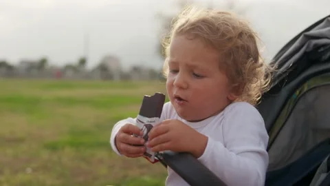 Little boy eats chocolate. A happy child eats sweets in baby stoller. Stock Footage 228010489