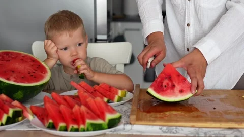 Little boy eats a juicy slice of watermelon, mom's hands cut the watermelon Stock Footage 290983410