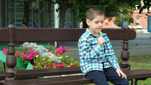 A little boy eats a lollipop while sitting on a bench in the city Video stock 250597928