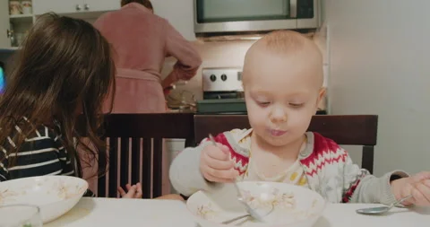 A little boy eats oatmeal with milk while sitting in a baby chair kitchen table. Stock Footage 229156357