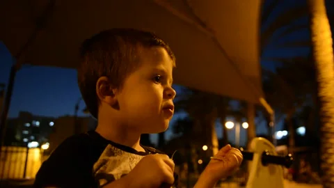 Little boy eats something in the park in the late evening.  low light soft focus Видео 140819162