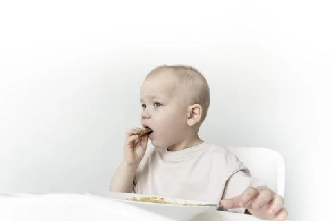 A little boy eats soup with bread on his own in a highchair against the backg Foto stock