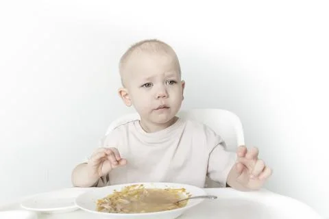 A little boy eats soup with bread on his own in a highchair against the backg Stock Photos
