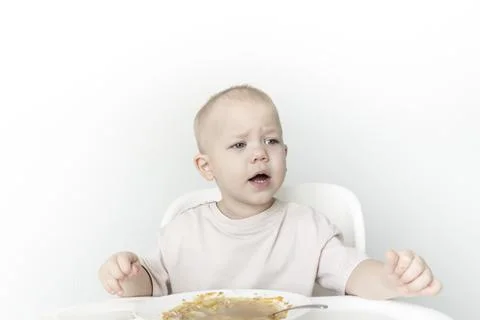 A little boy eats soup with bread on his own in a highchair against the backg Stock Photos