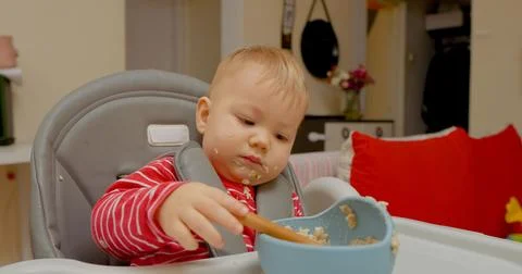 Little boy enjoyingly eats cereal in high chair during breakfast time Stock Photos