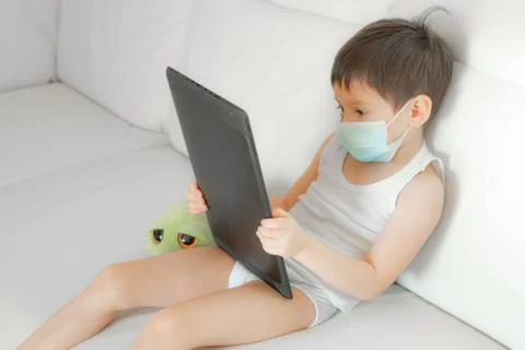 Little boy with face mask using a tablet Foto stock
