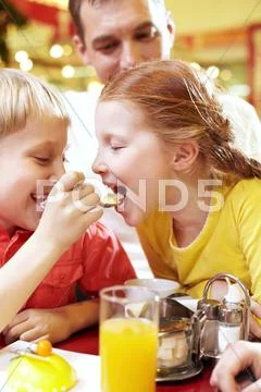 A little boy feeding his sister with a spoon in cafe Stock Photos