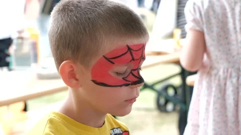 Little boy getting his face painted with a red superhero spider web mask at.. Vidéo 337404221