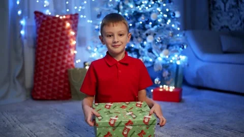 A little boy happily opens a gift under a shiny Christmas tree. Stock Footage 258583630