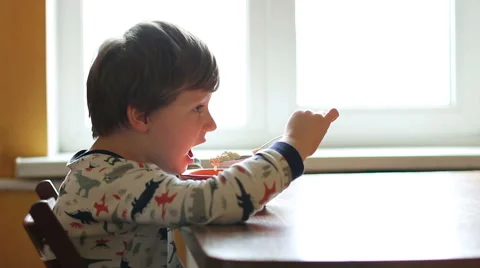 Little boy has breakfast. The boy eats porridge from orange plate at the table. Video stock 64673586