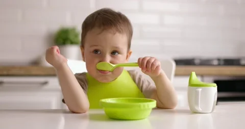 Little boy has breakfast in the kitchen. Happy baby eats porridge with spoon Stock Footage 154872559