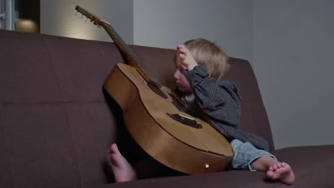 Little boy have fun with a big classical guitar on couch Stock Footage 150875378