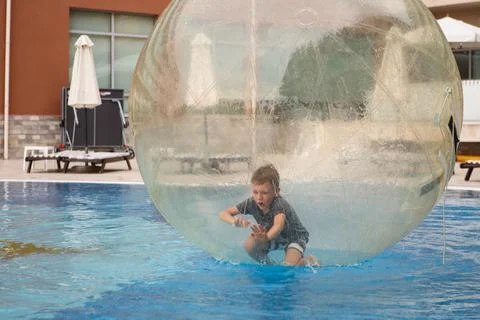 Little boy have fun inside big plastic balloon on the water of swimming pool  Stock Photos