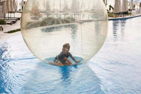 Little boy have fun inside big plastic balloon on the water of swimming pool  Stock Photos