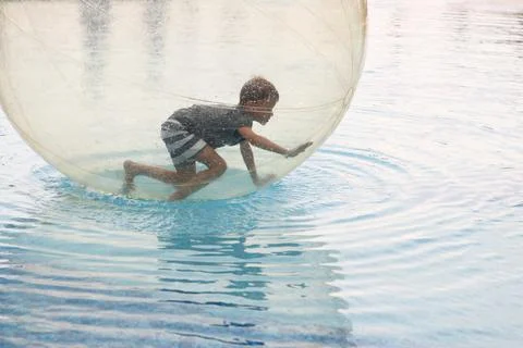 Little boy have fun inside big plastic balloon on the water of swimming pool  Stock Photos