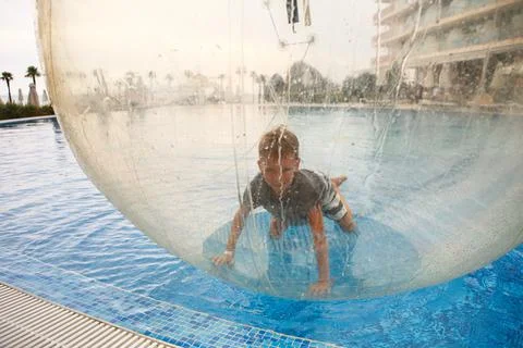 Little boy have fun inside big plastic balloon on the water of swimming pool  Stock Photos