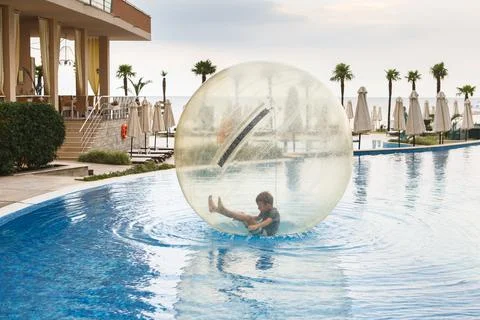 Little boy have fun inside big plastic balloon on the water of swimming pool  Stock Photos