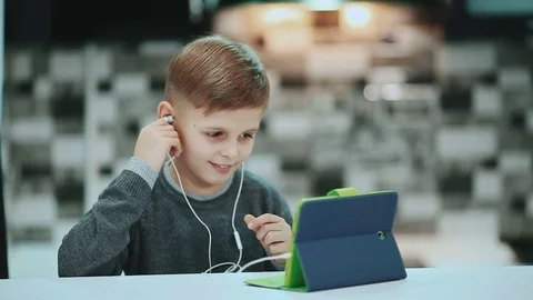 Little boy in headphones is using a digital tablet, sitting at home listening to Stock Footage 72198687