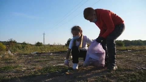 Little boy holding bag while his sister in gloves throwing paper waste in bag Stock Footage 322169758