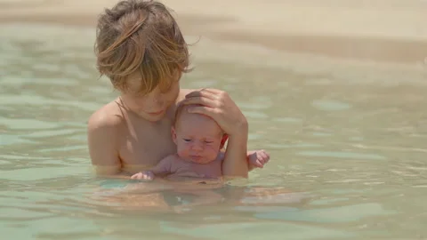 A little boy holds his tiny newborn brother in his hands while sitting in the Stock Footage 309312368