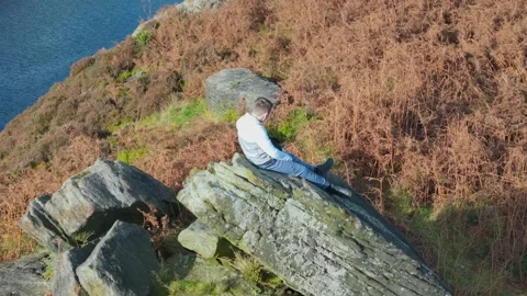 Little boy on a huge boulder, lost in contemplation. Aerial video slowly pa.. Vidéo 254161480