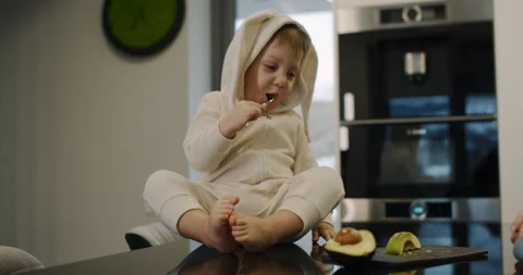 Little boy, hungry, eats an avocado in the kitchen with a fork. Slow motion. Video stock 150873817