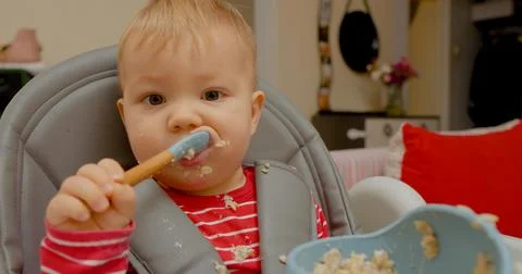 Little boy joyfully learning self-feeding at breakfast time in high chair Stock Photos