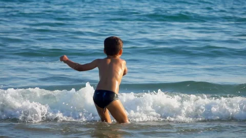 Little boy is jumping and rotating in a splashing sea waves Stock Footage 129117665
