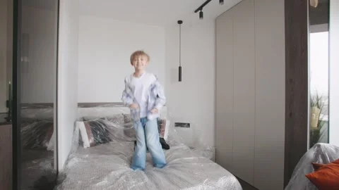 Little boy jumps on the bed surrounded by cardboard boxes, ready for their new Stock Footage 346226661