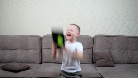 A little boy jumps on a big sofa rejoicing in winning a game on a tablet Stock Footage 165745141