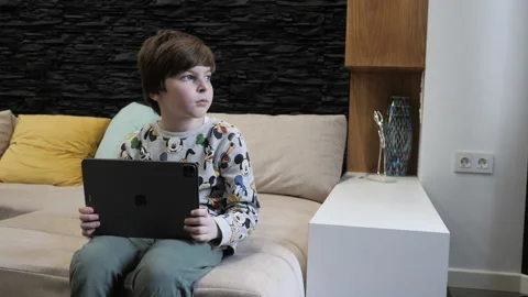 Little boy kid puts tablet on large bed and comes to window Video stock 148099284