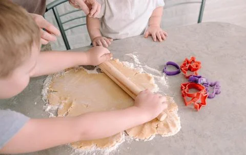 A little boy learns to roll out the dough with a rolling pin on the table the Stock Photos