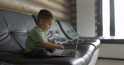 Little boy learns to type on a laptop keyboard while sitting on a sofa in Video stock 197441700