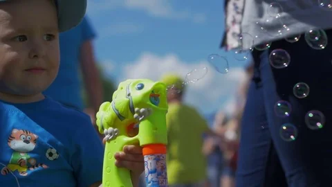 Little boy lets bubbles out of a gun and looks into the camera Stock Footage 82405350