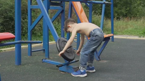 Little boy lifting heavy weight on the outdoor sports ground Stock Footage 93667589