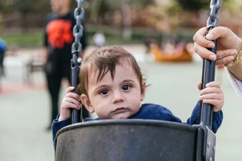 Little boy looking at camera while sitting in the swing at the playground in the Stock Photos