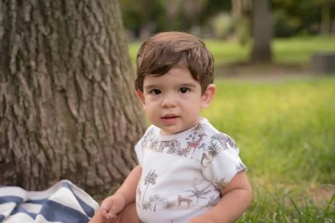 Little boy looking at the camera while sitting outdoors in a park. Stock Photos
