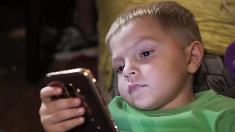 Little boy looking at mobile phone screen on sofa. gadget addiction Stock Footage 285023293
